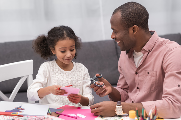 smiling african american father and daughter cutting paper for greeting card on mothers day - Foto, afbeelding