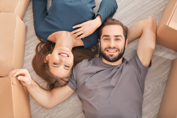 Happy young couple lying on floor in their new home near moving boxes - Zdjęcie, obraz