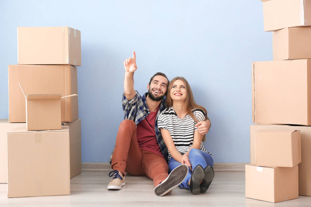 Young couple with moving boxes on floor in room - Фото, изображение