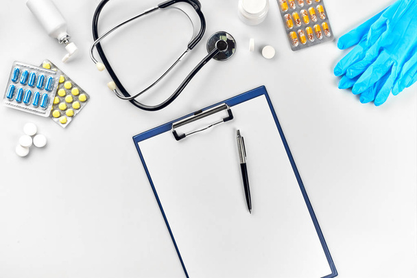 Sprzęt medyczny: pigułki, niebieskie rękawice, termometr i stetoskop, białe puste piórem na białym tle. Widok z góry. Miejsce - Zdjęcie, obraz