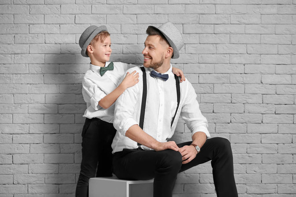 Father and son in elegant suits against brick wall - Zdjęcie, obraz