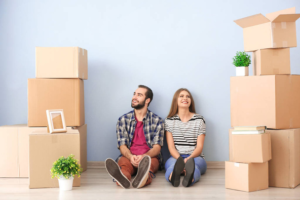 Young couple with moving boxes on floor in room - Фото, изображение