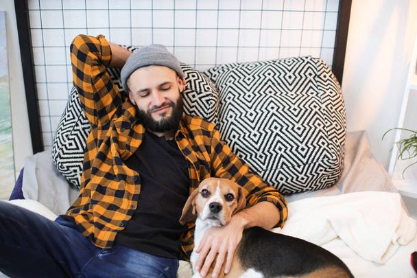 Handsome young hipster with his dog resting on bed at home - Photo, image
