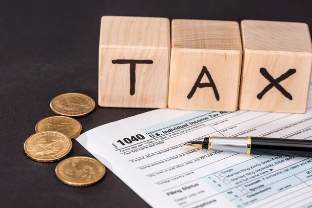 1040 formulario de impuestos, cubos de madera impuesto pluma y moneda en negro
 - Foto, imagen