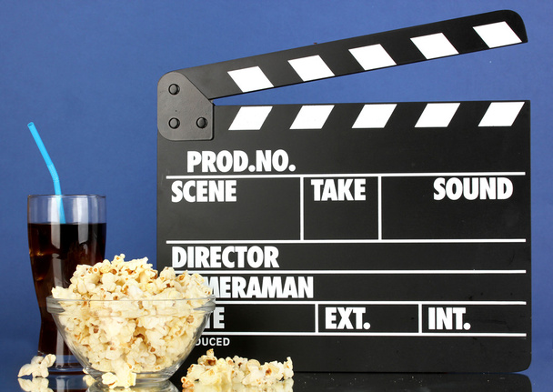 Movie clapperboard, cola and popcorn on blue background - Photo, Image