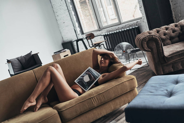 gorgeous woman covered with magazine lying on sofa at home - Fotoğraf, Görsel