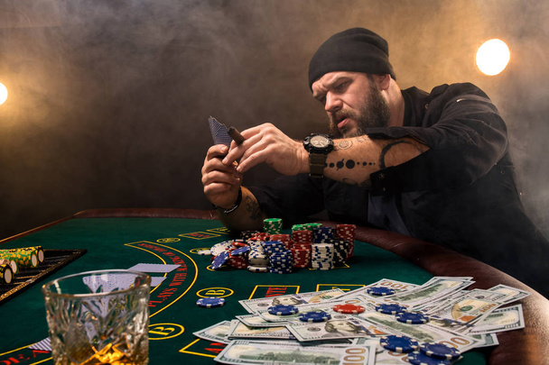 Szakállas férfi szivar és üveg egy kaszinó póker asztalnál. Szerencsejáték, kártya és a rulett. - Fotó, kép