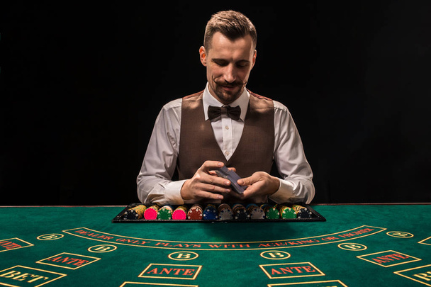 Portrait d'un croupier tient des cartes à jouer, des jetons de jeu sur la table. Fond noir
 - Photo, image