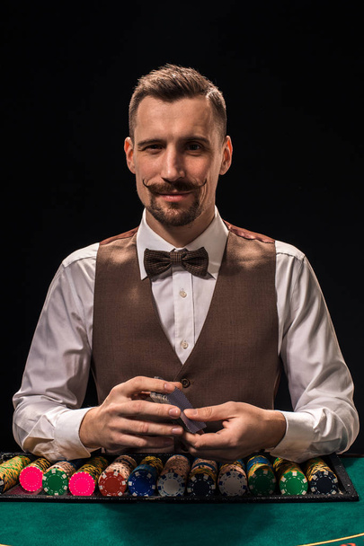 Portret van een croupier houdt speelkaarten, gokken chips op tafel. Zwarte achtergrond - Foto, afbeelding