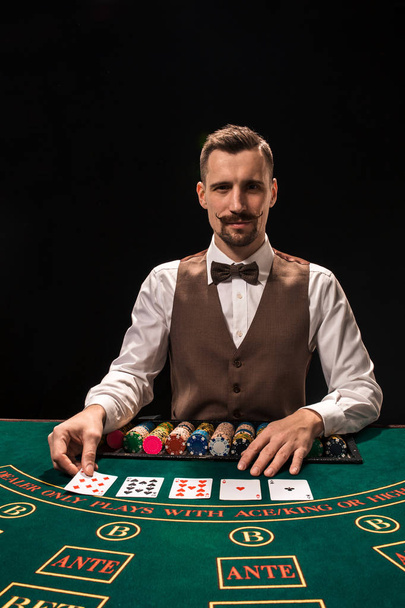Πορτρέτο του ένα κρουπιέρης κρατά παίζοντας χαρτιά, τυχερών παιχνιδιών μάρκες στο τραπέζι. Μαύρο φόντο - Φωτογραφία, εικόνα