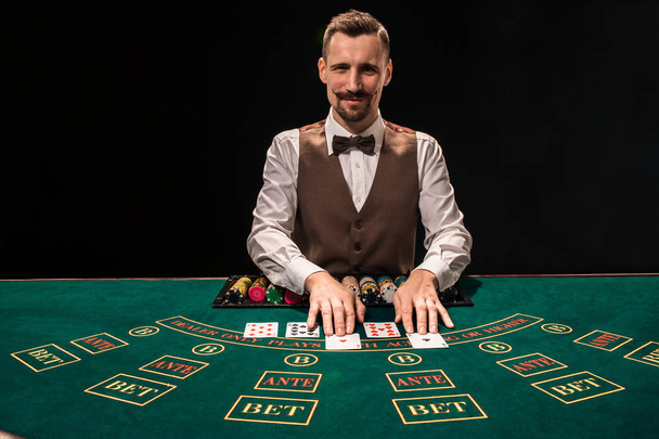 Retrato de un croupier es la celebración de cartas, fichas de juego en la mesa. Fondo negro
 - Foto, Imagen