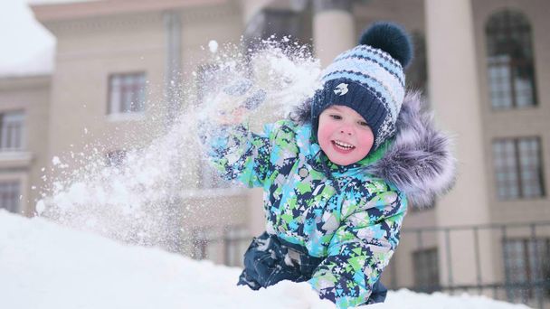 Małe dziecko gra na ośnieżonych górskich, wyrzuca śnieg i śmieje się. Słoneczny dzień mroźny. Gry i zabawy na świeżym powietrzu. - Zdjęcie, obraz