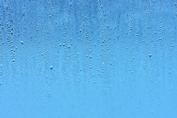 Окно стекло с высокой влажностью конденсата, большие капли стекают вниз, холодный тон. Природные капли воды фон
 - Фото, изображение