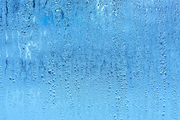 Ventana de vidrio con condensación de alta humedad, gotas grandes fluyen hacia abajo, tono frío. Fondo de gota de agua natural
 - Foto, imagen