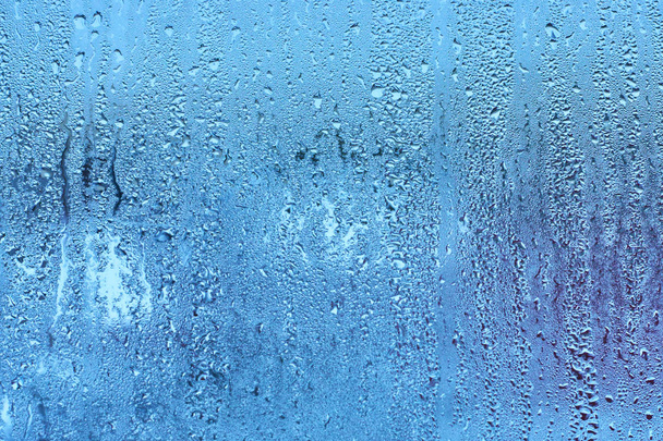 Vensterglas met condensatie hoge vochtigheid, stroom van de grote druppels naar beneden, koude Toon. Natuurlijke water drop achtergrond - Foto, afbeelding