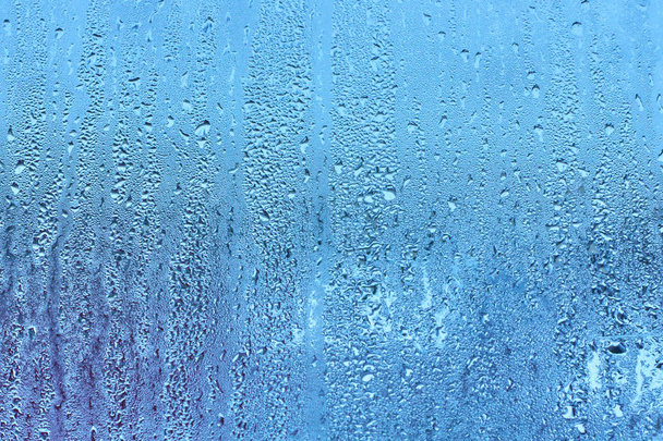 Окно стекло с высокой влажностью конденсата, большие капли стекают вниз, холодный тон. Природные капли воды фон
 - Фото, изображение