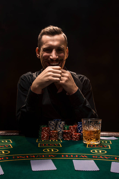 Man is het spelen van poker met een sigaar en een whiskey. Een man winnen van alle chips op tafel met dikke sigarettenrook. - Foto, afbeelding