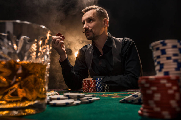 男は、葉巻とウイスキーとポーカーをプレイです。男の太いタバコの煙とテーブルの上のすべてのチップを獲得. - 写真・画像