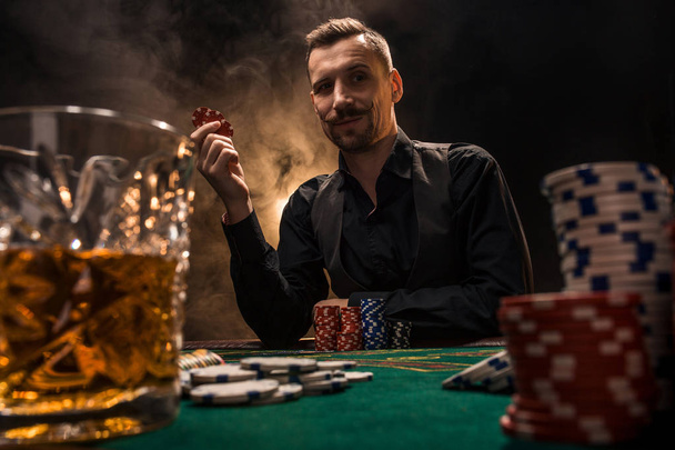 L'uomo sta giocando a poker con un sigaro e un whisky. Un uomo che vince tutte le patatine sul tavolo con fumo di sigaretta denso
. - Foto, immagini