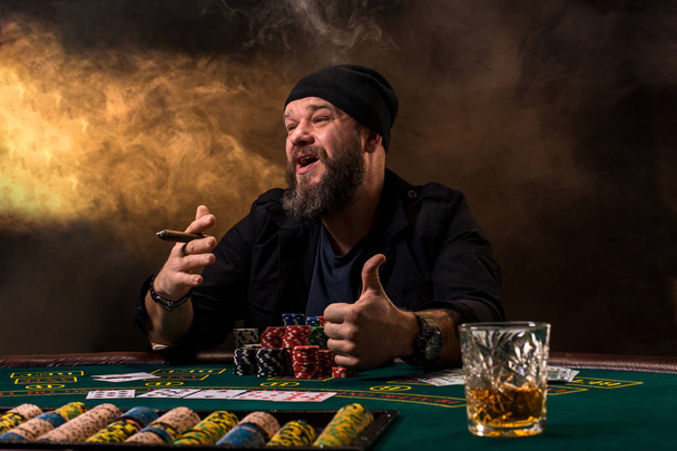Чоловік грає в покер з сигарою і віскі. Чоловік виграє всі фішки на столі з товстим сигаретним димом
. - Фото, зображення