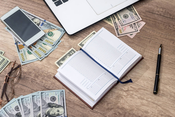 Laptop, Notizbuch, Stift, Dollar, Telefon auf Holztisch - Foto, Bild