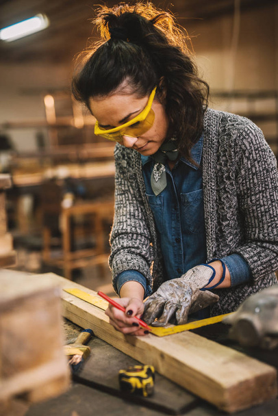 carpintero mujer trabajadora que trabaja con la regla y hacer marcas en la madera en el taller
 - Foto, Imagen