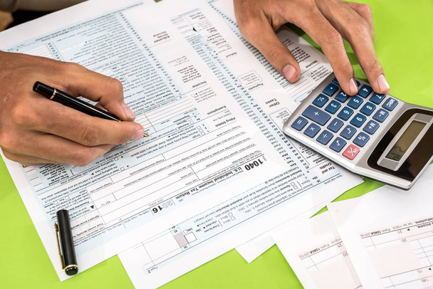 Mann füllt Steuerformular mit Stift und Taschenrechner aus - Foto, Bild