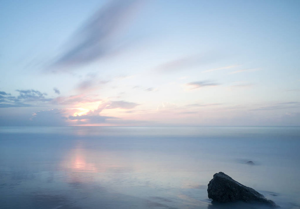 Ανατολή ηλίου ήρεμο ωκεανό με ένα μεγάλο βράχο στο πρώτο πλάνο - Φωτογραφία, εικόνα