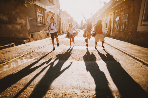 Grup genç mutlu arkadaşıyla şehirde seyahat ve güneşli Caddesi üzerinde atlama - Fotoğraf, Görsel