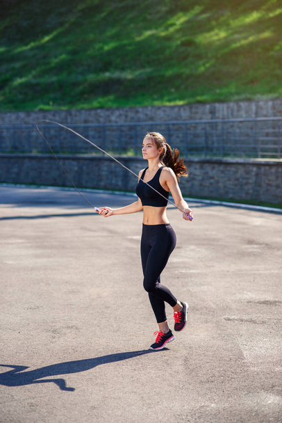 Athlete woman jumping with skipping rope at stadium. Active fitness female doing exercises outdoor. Fitness concept. Healthy lifestyle. - Fotó, kép