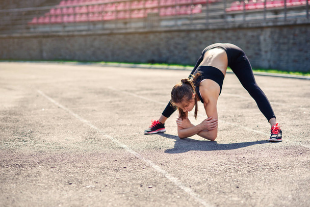 Fitness girl doing stretching on the sadium before training. Fitness female athlete doing a warm up before her strength training cardio workout. - Fotó, kép