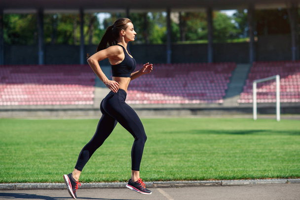 Young fitness woman running on a stadium track. Athlete girl doing exercises on the training at stadium. Healthy active lifestyle. - Foto, Imagem