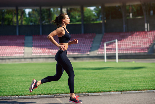 Young fitness woman running on a stadium track. Athlete girl doing exercises on the training at stadium. Healthy active lifestyle. - 写真・画像