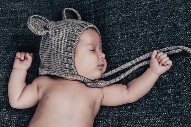A newborn baby in a cap sleeps on a gray plaid - Fotoğraf, Görsel