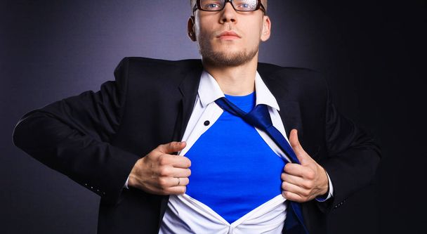 Jonge zakenman handelt zoals een super held en scheuren zijn overhemd, geïsoleerd op grijze achtergrond - Foto, afbeelding