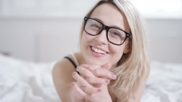 4 k atrakcyjna kobieta, relaks w domu, leżąc na łóżku i uśmiecha się do kamery - Materiał filmowy, wideo