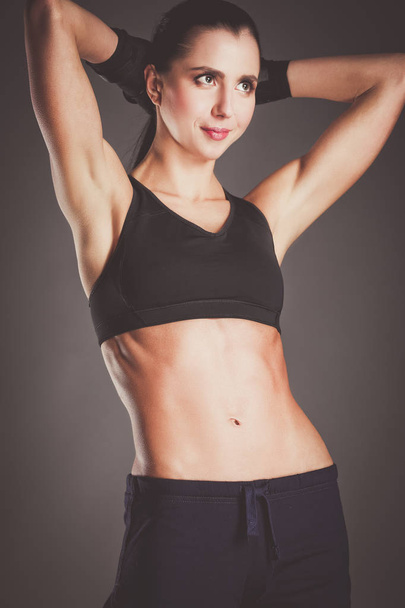 Muscular young woman posing in sportswear against black background - Foto, imagen