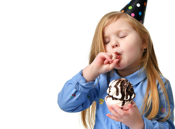 Three years girl kid eat sweet chocolate cake celebrating in birthday cap isolated  - Zdjęcie, obraz