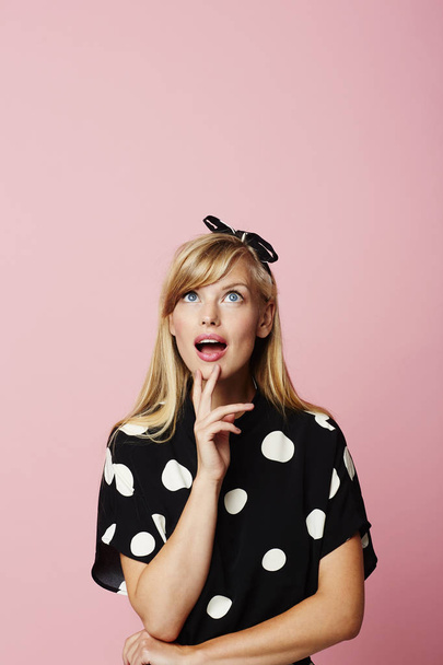Portrait of young surprised woman looking up wearing polka dot dress - Fotó, kép