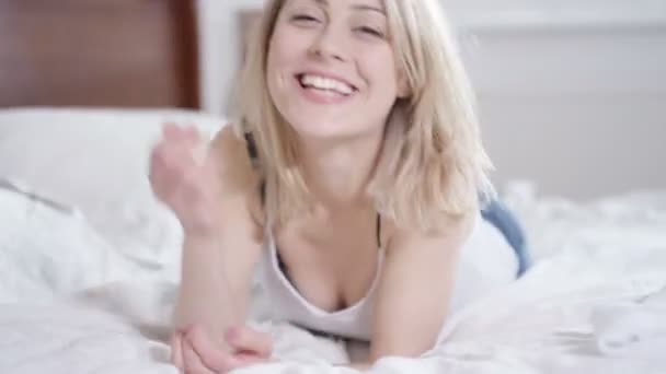 4K Attractive woman relaxing at home, lying on bed and smiling to camera - Záběry, video