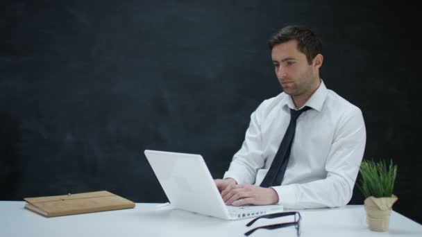 4K Pensive businessman working on laptop with chalkboard background - Video