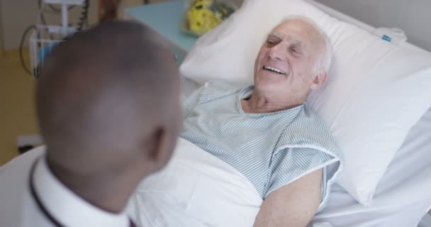 4K Friendly doctor talking to elderly patient at his bedside - Materiaali, video