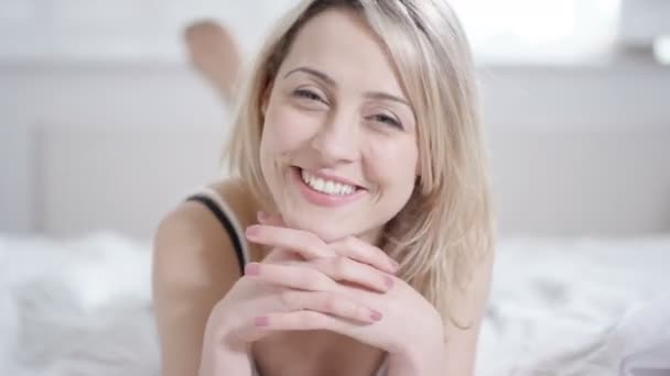 4K Attractive woman relaxing at home, lying on bed and smiling to camera - Séquence, vidéo