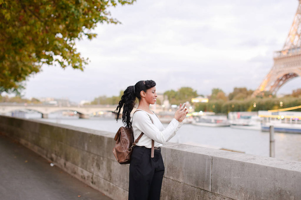 Νεαρή γυναίκα στέκεται πάνω σε ανάχωμα στο Παρίσι και βλέποντας φωτογραφίες  - Φωτογραφία, εικόνα