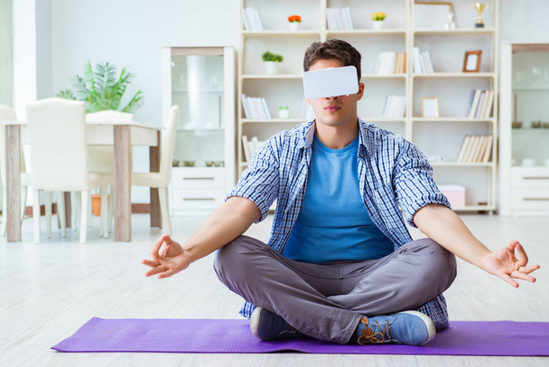 Мужчина в очках виртуальной реальности медитирует на полу в центре - Фото, изображение