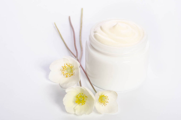 Schattige bloemen en een pot van natuurlijke lichaam crème geïsoleerd op wit  - Foto, afbeelding