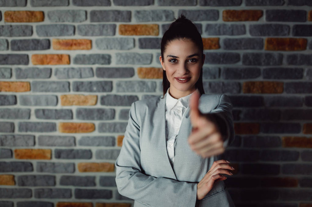 Happy businesswoman showing thumb up over brick wall. - Photo, image