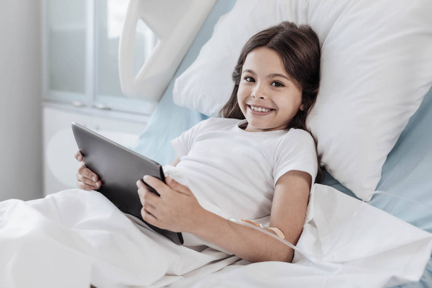 Brave girl playing on touchpad while lying in hospital bed - Фото, зображення