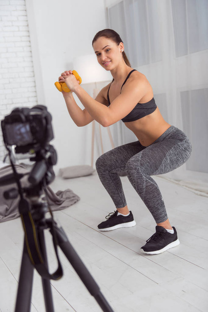 Joyful blogger squatting with hand weights for cam - Foto, imagen