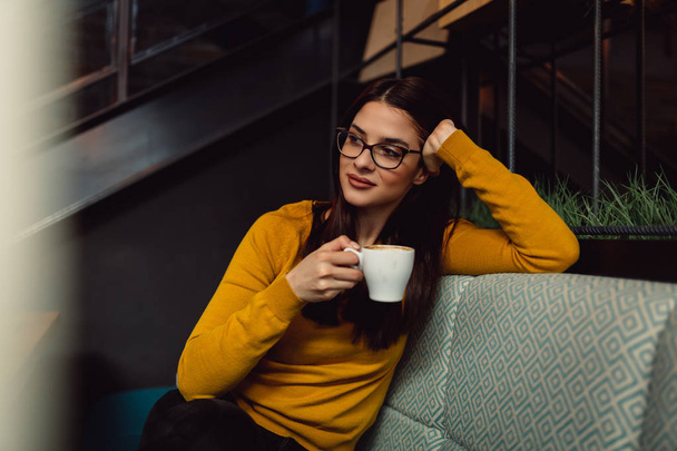 Portret van een mooie jonge brunette vrouw genieten van koffie. - Foto, afbeelding